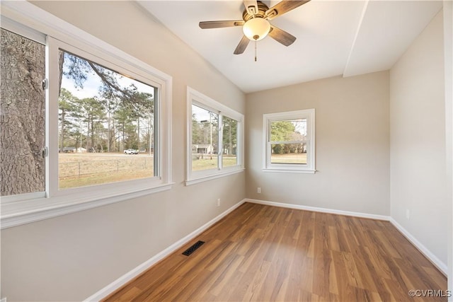 spare room with a ceiling fan, visible vents, baseboards, and wood finished floors