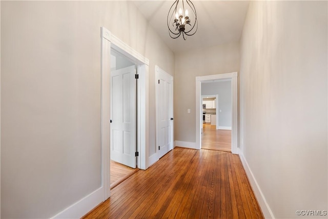 corridor featuring baseboards, a chandelier, and hardwood / wood-style floors