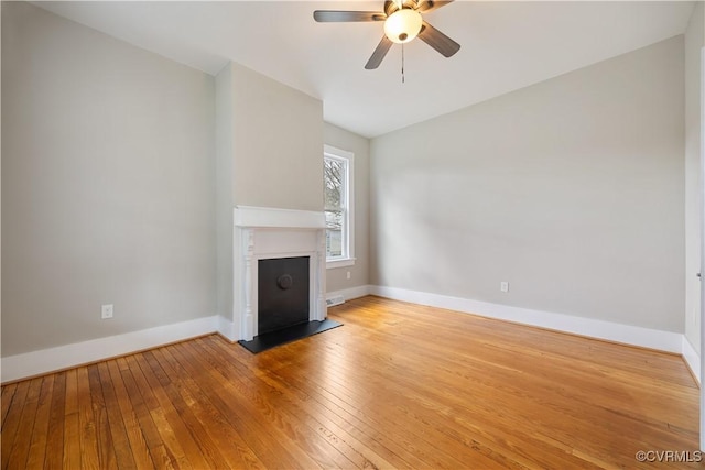 unfurnished living room with a ceiling fan, wood-type flooring, a fireplace with raised hearth, and baseboards