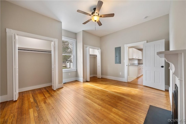 unfurnished bedroom featuring light wood finished floors, electric panel, baseboards, and multiple closets