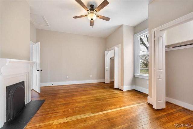 unfurnished bedroom featuring light wood finished floors, baseboards, a ceiling fan, a fireplace, and two closets