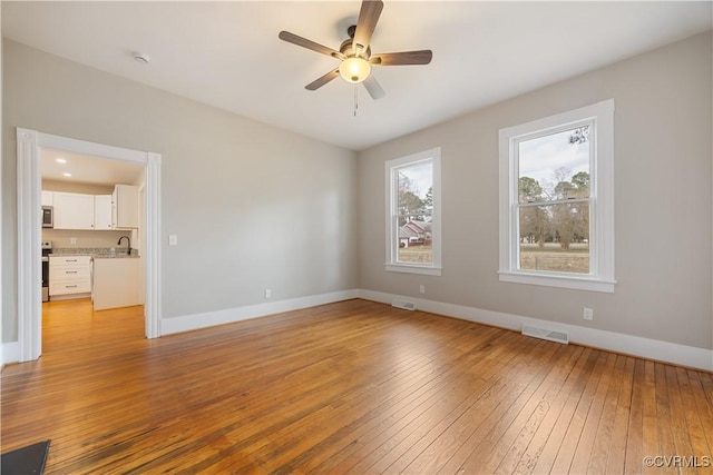 unfurnished room featuring light wood-type flooring, visible vents, a sink, and baseboards