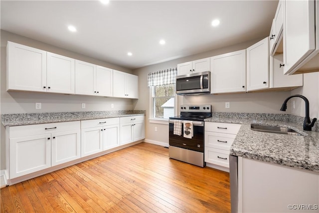 kitchen with appliances with stainless steel finishes, light wood-style floors, white cabinets, and a sink