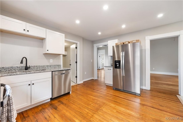 kitchen featuring light wood finished floors, appliances with stainless steel finishes, white cabinetry, a sink, and recessed lighting