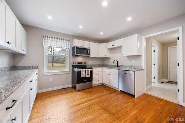 kitchen with stainless steel appliances, recessed lighting, white cabinetry, a sink, and light wood-type flooring