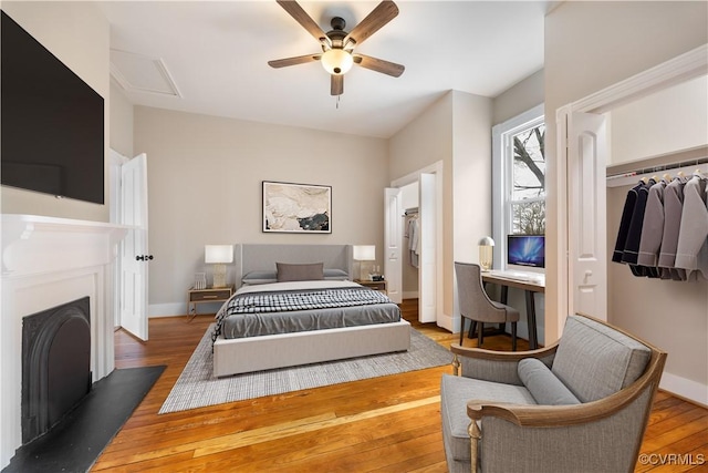 bedroom featuring a fireplace, wood finished floors, a ceiling fan, and baseboards