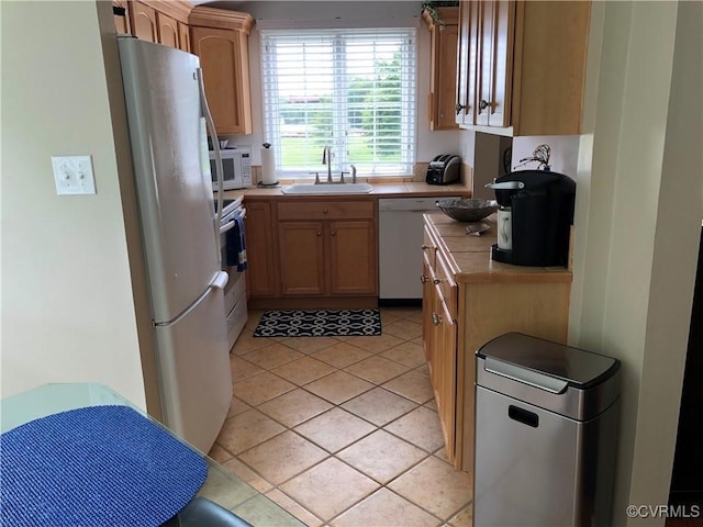 kitchen with light tile patterned floors, white appliances, a sink, and tile counters