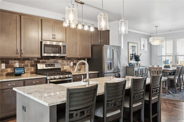 kitchen featuring decorative backsplash, an island with sink, dark wood-style flooring, stainless steel appliances, and crown molding