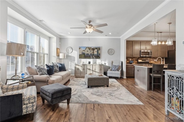 living room with ornamental molding, visible vents, ceiling fan, and wood finished floors