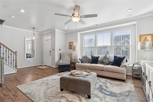 living room with baseboards, ceiling fan, stairway, wood finished floors, and crown molding