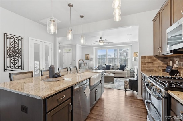 kitchen featuring dark wood-style flooring, decorative light fixtures, stainless steel appliances, decorative backsplash, and a sink