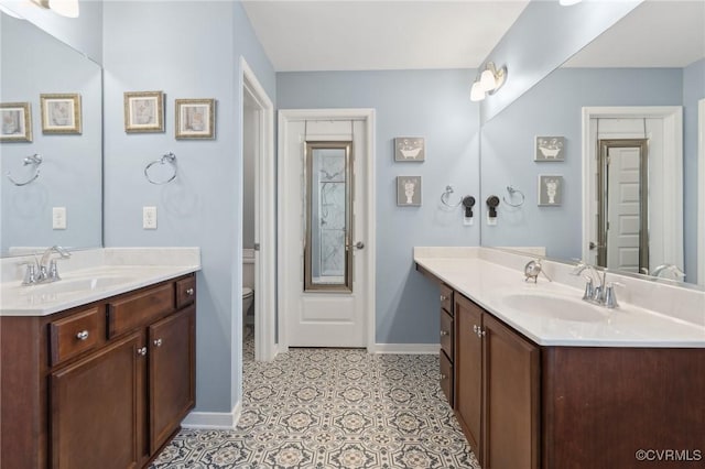 full bathroom with toilet, baseboards, two vanities, and a sink