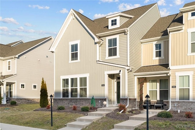 multi unit property featuring roof with shingles, a front yard, and brick siding