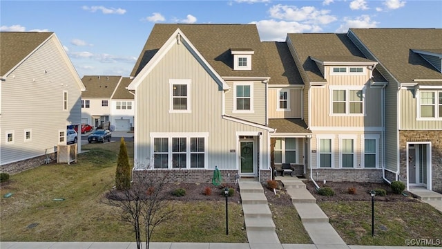 townhome / multi-family property featuring a shingled roof, a residential view, a front lawn, board and batten siding, and brick siding