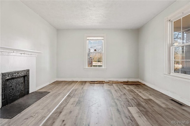 unfurnished living room featuring a textured ceiling, a premium fireplace, visible vents, and wood finished floors