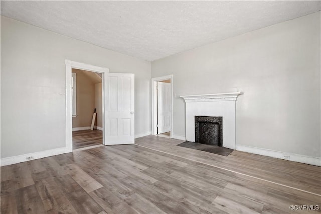 unfurnished living room with a fireplace with flush hearth, a textured ceiling, baseboards, and wood finished floors