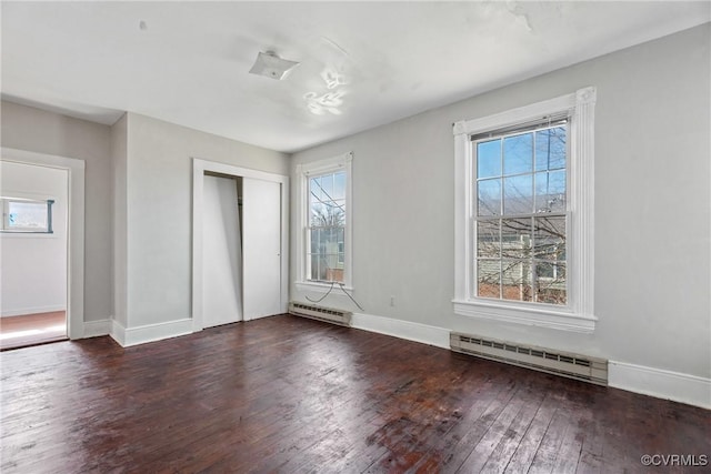 unfurnished bedroom featuring a baseboard heating unit, multiple windows, and hardwood / wood-style flooring