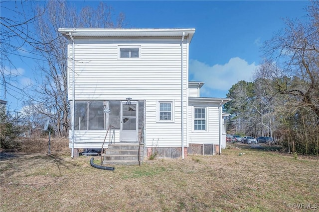 rear view of property featuring entry steps, a sunroom, and a lawn