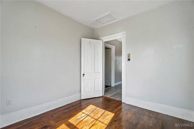 spare room with attic access, wood-type flooring, and baseboards