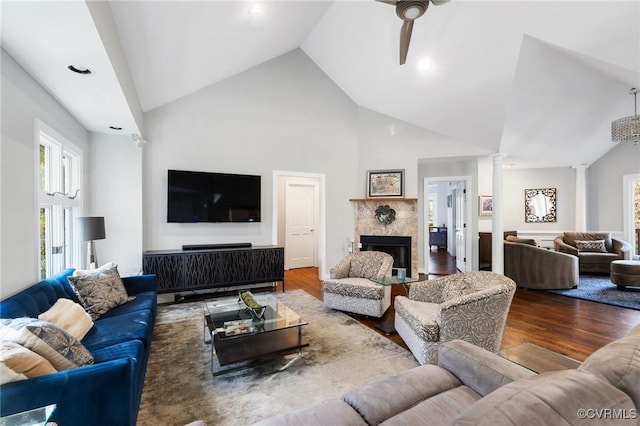 living area with decorative columns, a tile fireplace, ceiling fan, wood finished floors, and high vaulted ceiling