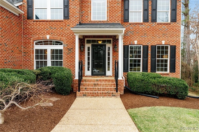 entrance to property with a shingled roof and brick siding