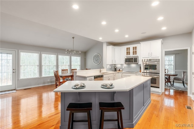 kitchen with appliances with stainless steel finishes, a peninsula, a sink, light countertops, and backsplash