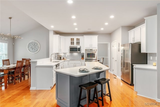 kitchen featuring white cabinets, a breakfast bar, a peninsula, stainless steel appliances, and light countertops