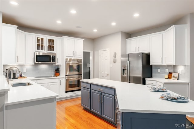 kitchen with stainless steel appliances, a sink, white cabinets, a center island, and light wood finished floors