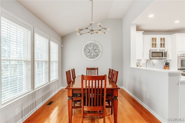 dining room with lofted ceiling, a chandelier, visible vents, baseboards, and light wood-style floors