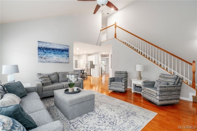 living room featuring light wood-style flooring, a ceiling fan, a towering ceiling, stairs, and baseboards