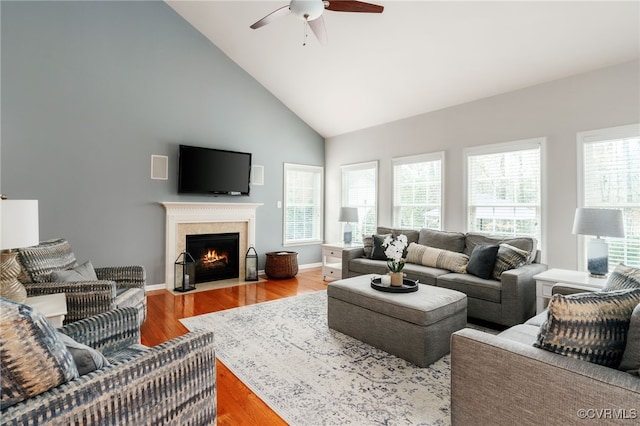 living area with a healthy amount of sunlight, a fireplace with flush hearth, high vaulted ceiling, and wood finished floors