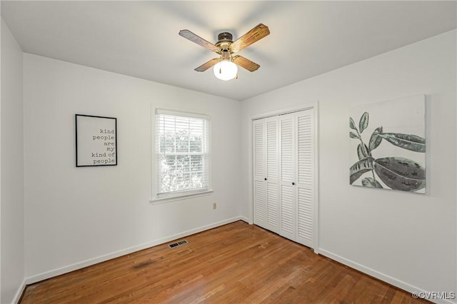 unfurnished bedroom with a closet, visible vents, baseboards, and wood finished floors