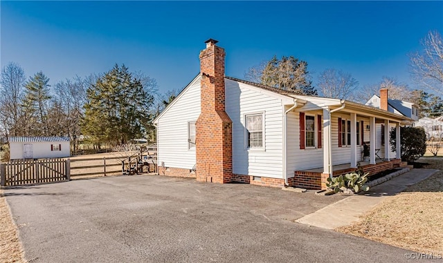 view of side of property with crawl space, a chimney, fence, and a porch