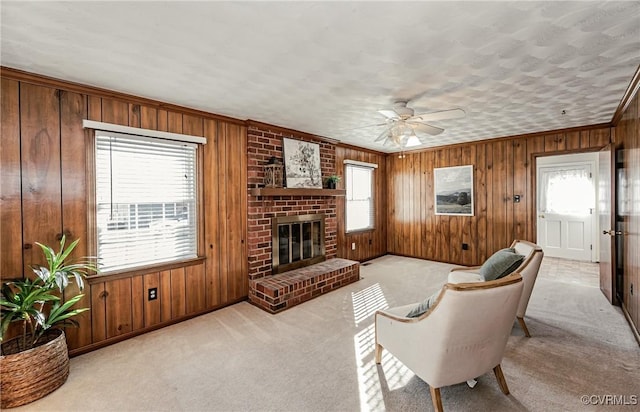 living area with light carpet, wood walls, a fireplace, a ceiling fan, and ornamental molding