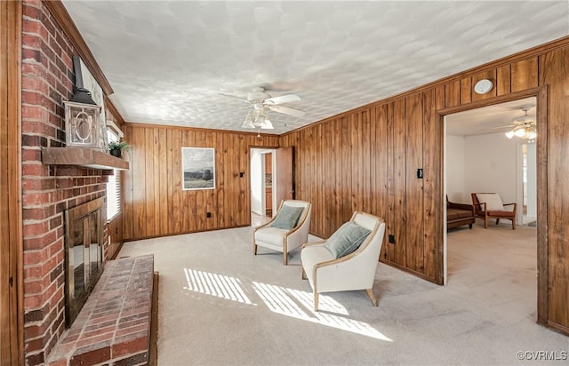 living area featuring wooden walls, a fireplace, a ceiling fan, and light colored carpet