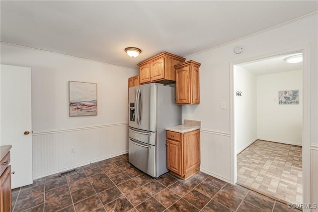 kitchen featuring brown cabinets, stainless steel refrigerator with ice dispenser, light countertops, and wainscoting