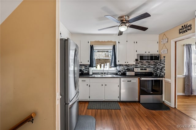 kitchen featuring dark wood-style flooring, stainless steel appliances, dark countertops, tasteful backsplash, and a sink