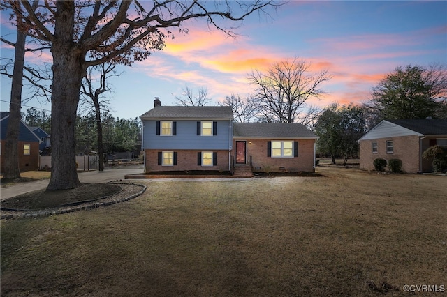 tri-level home featuring crawl space, a chimney, a front lawn, and brick siding