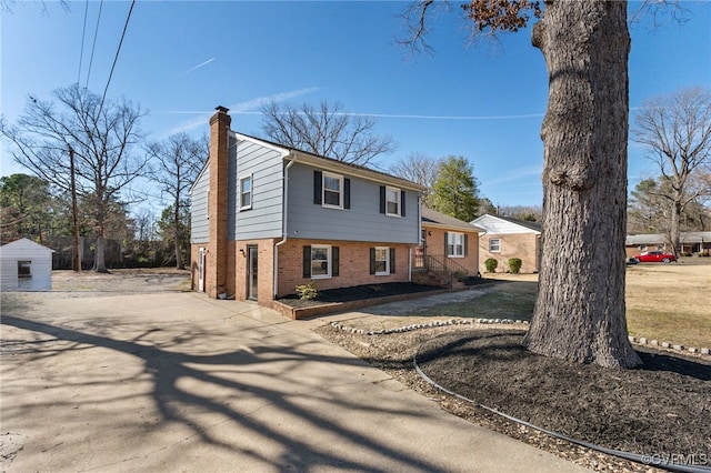 split level home featuring concrete driveway, brick siding, and a chimney