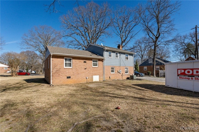 rear view of house featuring a yard, brick siding, crawl space, and a chimney