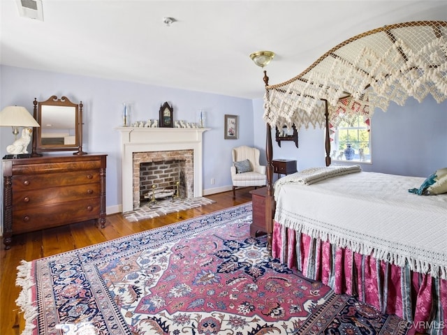 bedroom with visible vents, a fireplace, baseboards, and wood finished floors