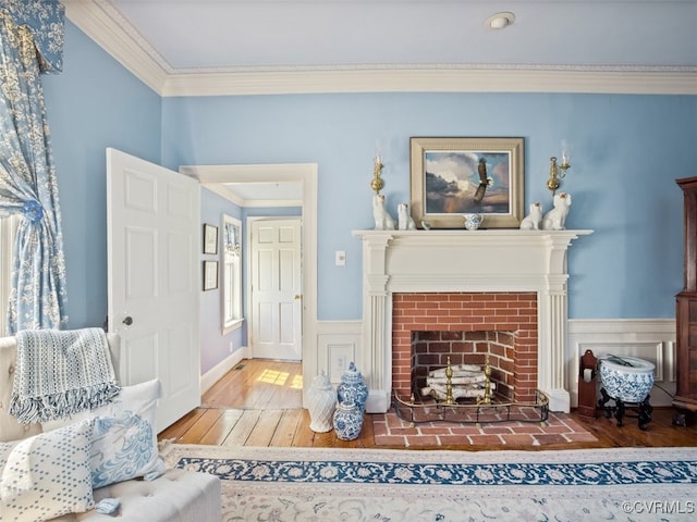 living area featuring a brick fireplace, wainscoting, crown molding, and wood finished floors