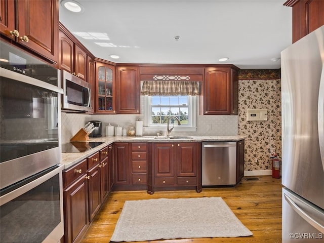 kitchen featuring appliances with stainless steel finishes, light wood-style floors, a sink, light stone countertops, and wallpapered walls