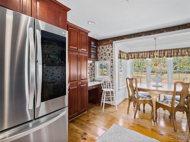 kitchen with hanging light fixtures, light wood finished floors, smart refrigerator, glass insert cabinets, and wallpapered walls