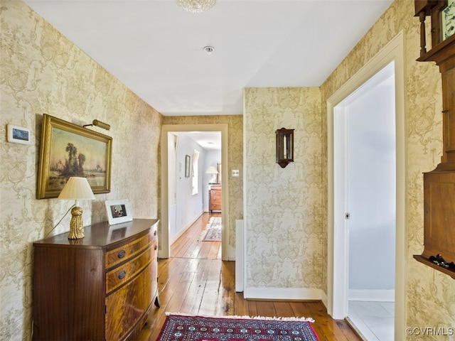 hall with baseboards, wood-type flooring, and wallpapered walls