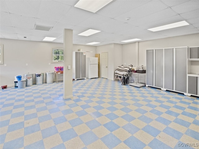 basement featuring baseboards, visible vents, a drop ceiling, and freestanding refrigerator