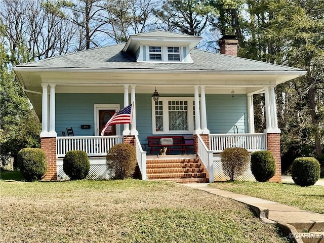 bungalow featuring covered porch, a shingled roof, a chimney, and a front yard