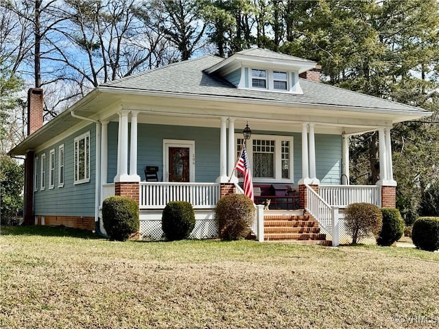 view of front of home with covered porch, a shingled roof, a chimney, and a front yard