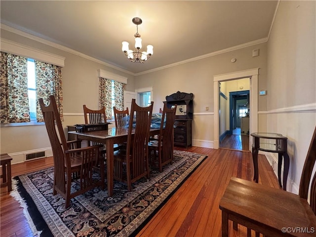 dining space featuring crown molding, wood-type flooring, visible vents, and a notable chandelier