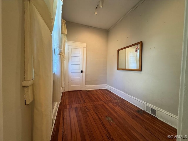 hallway featuring rail lighting, dark wood finished floors, visible vents, and baseboards